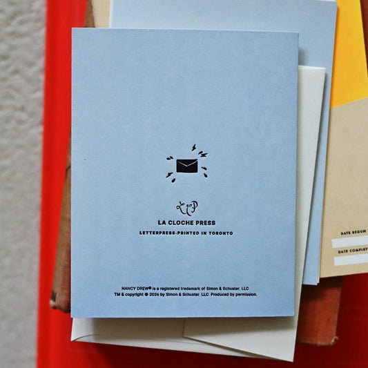 Back of a pale blue greeting card with black letterpress text, including the La Cloche Press branding, information that the card was printed in Toronto, and a cute sweaty envelope.